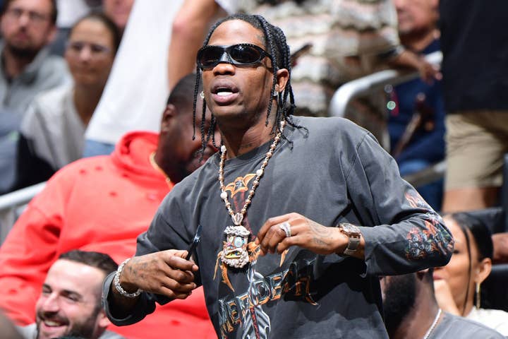 Travis Scott in a graphic tee and chains gestures at an event; focus on his casual style, not his sneakers