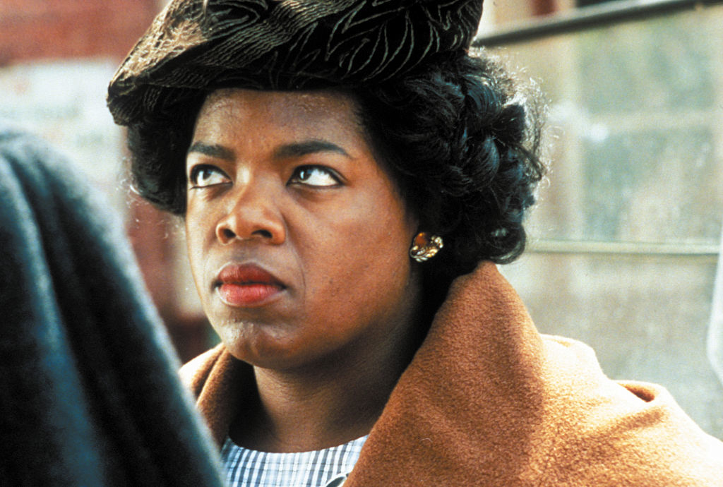 Oprah Winfrey portraying Sofia in &quot;The Color Purple&quot;, wearing a hat and a brown coat, looking perturbed