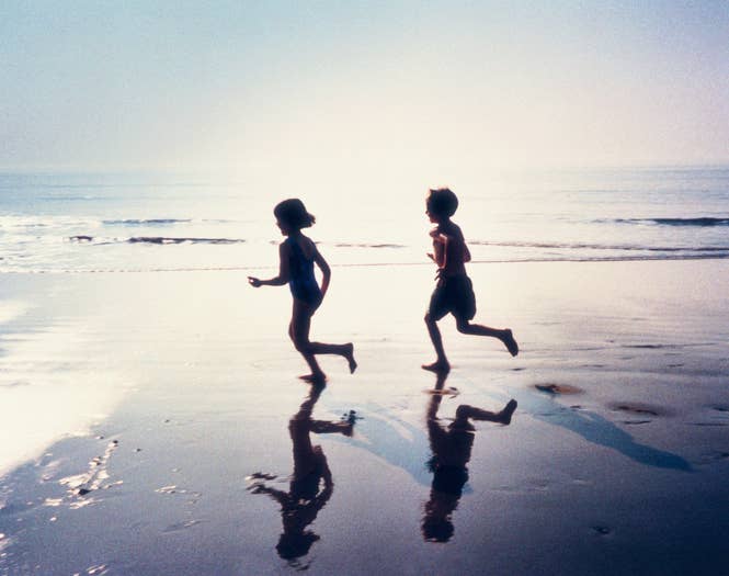 Two children running on the beach, their silhouettes reflected on the wet sand