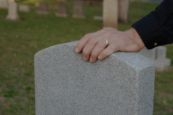 Person&#x27;s hand with a ring resting on a tombstone, indicating mourning or remembrance