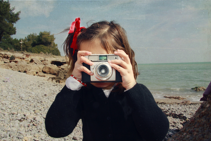 Child taking a photo with a vintage camera on a beach