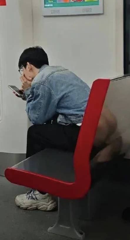 Person sitting on a public bench, hunched over their phone