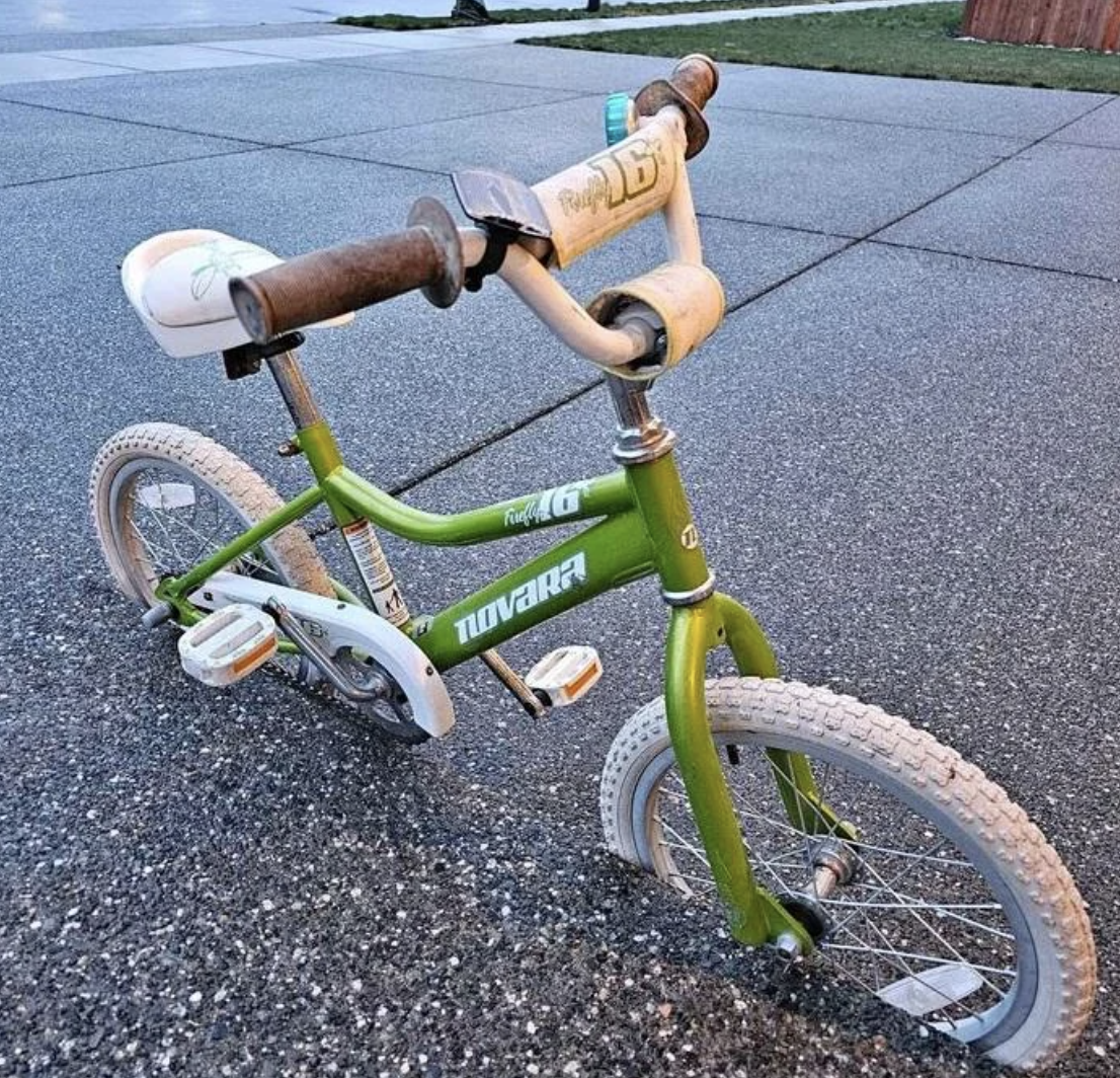 Child&#x27;s green and white bicycle parked on a sidewalk