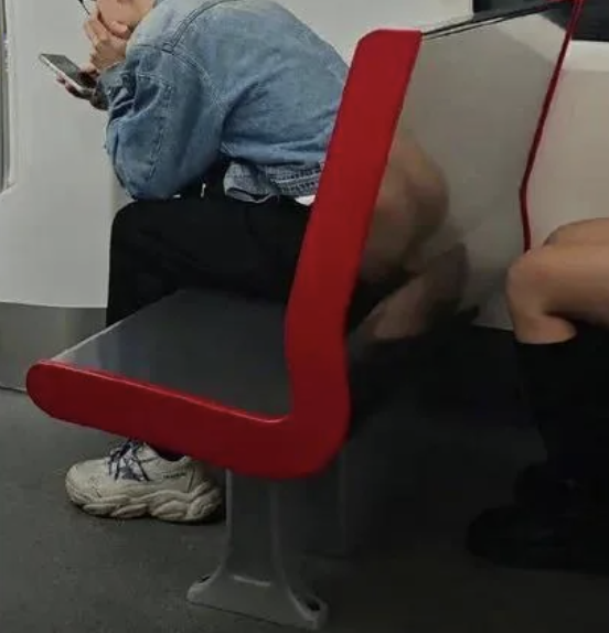 Person sitting on a red and grey seat on public transport, using a smartphone, another passenger beside, details obscured