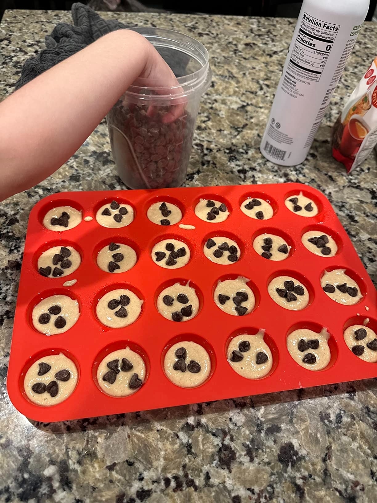 Hand placing chocolate chips on cookie dough balls in a red baking tray