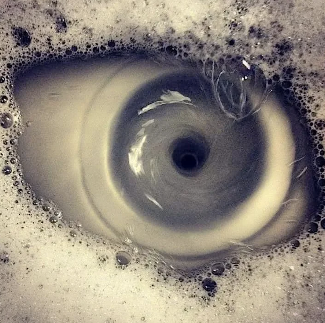 Close-up of a swirling vortex formation in sudsy water going down a drain