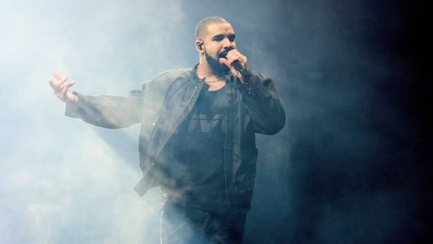 Drake performing on stage with a microphone, wearing a jacket and a T-shirt