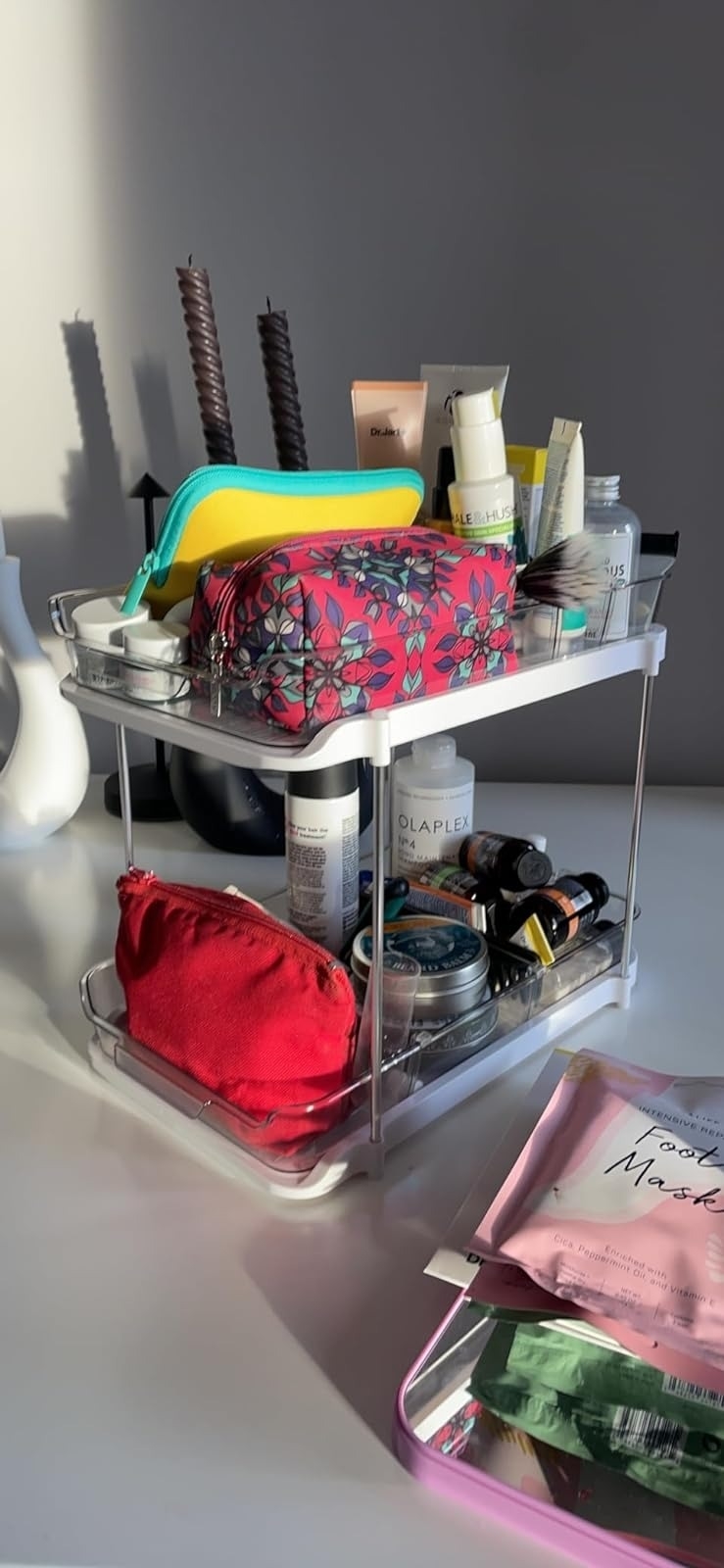 Transparent organizer with various skincare products and a patterned makeup bag on a vanity