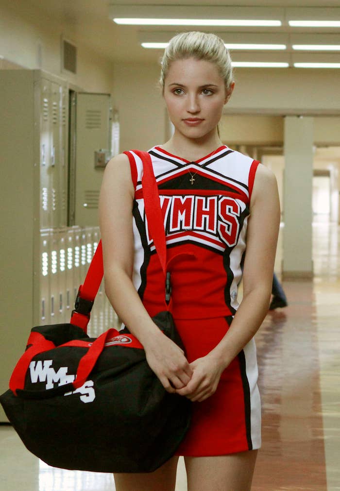 Quinn Fabray, character from Glee, standing in a hallway wearing a cheerleading outfit and holding a gym bag