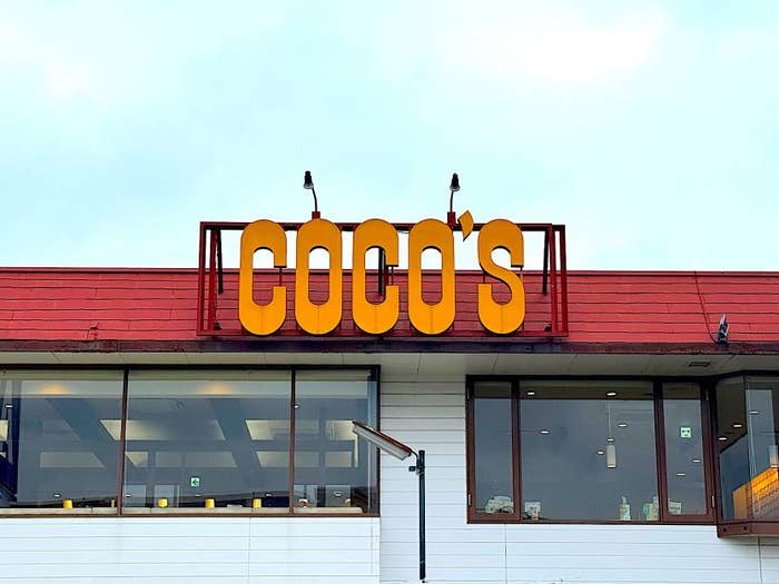 Sign with "COCO'S" on top of a building against a cloudy sky. Two birds perched on the sign