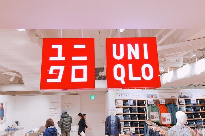 店内に吊るされた「ユニクロ」の赤い看板２つ。マネキンと買い物をする人々がいる。