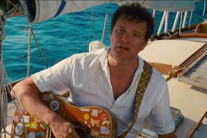 Man sitting on a boat holding a guitar with stickers, looking forward