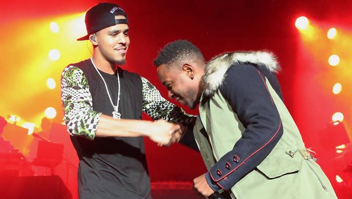 Two artists onstage interacting, one in a patterned jacket and cap, the other in a winter coat with fur hood