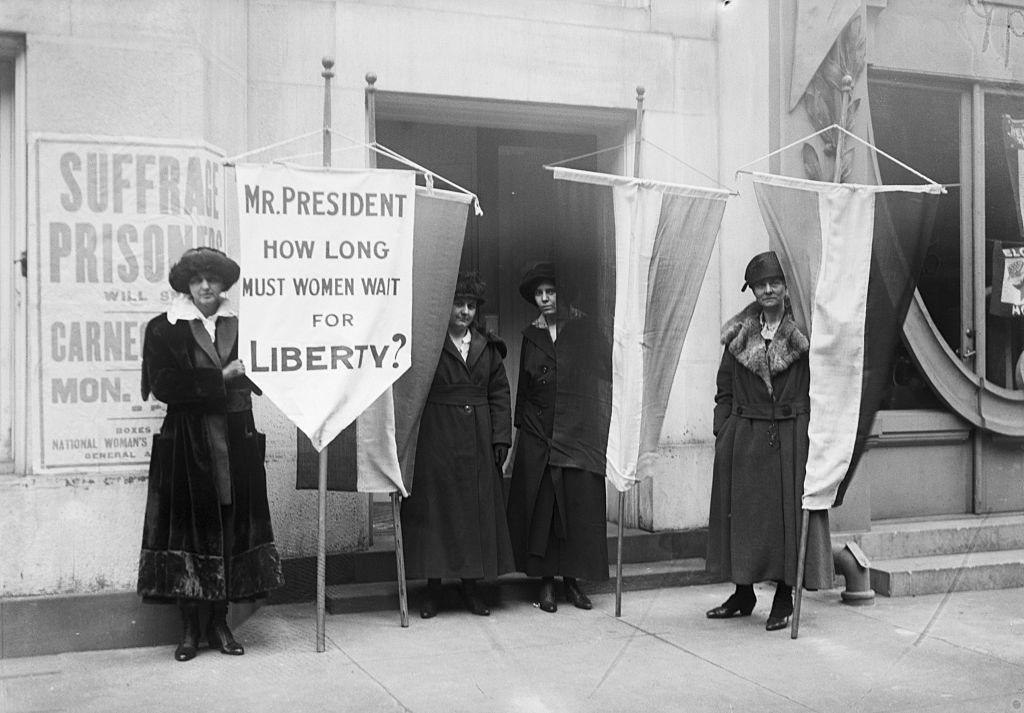 Women suffragists hold banners questioning the President about women&#x27;s liberty next to a building