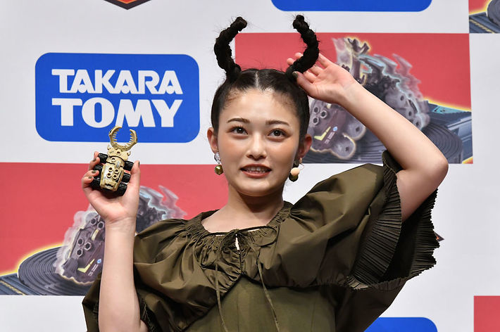 女性がブラウスを着て、頭に角のような装飾をしている。手に小さいおもちゃを持っている。