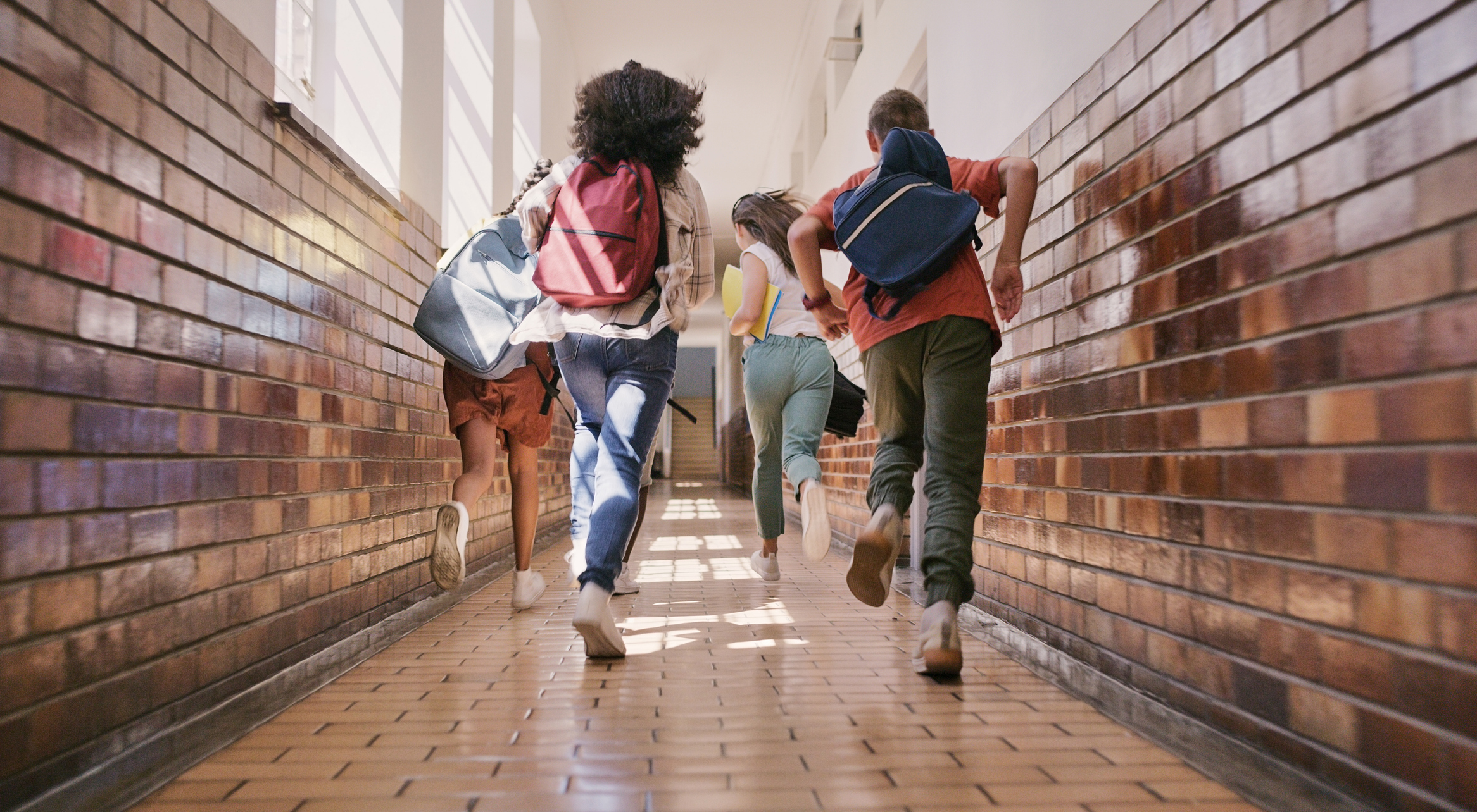 Children with backpacks running through a school hallway