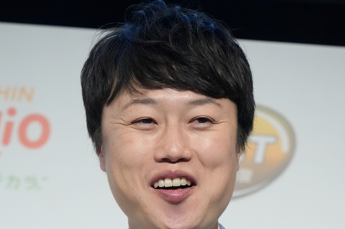 男性がグレーのスーツと緑のストライプのネクタイを着用し、笑顔でカメラを見ています。