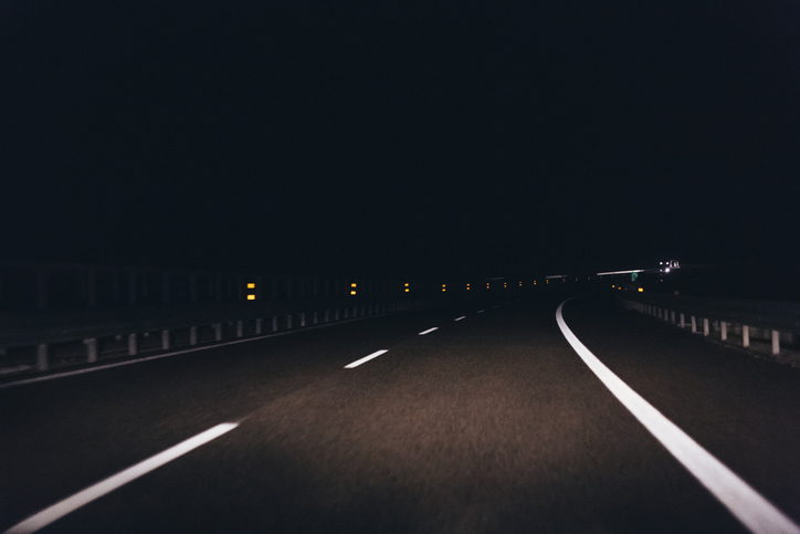 A dark highway at night with reflective lane markings and lights in the distance
