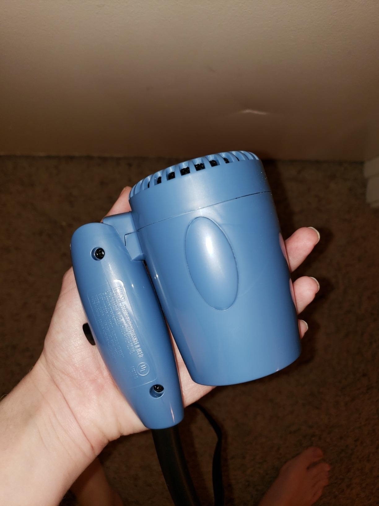 a reviewer holding the blue hair dryer folded in half in one hand