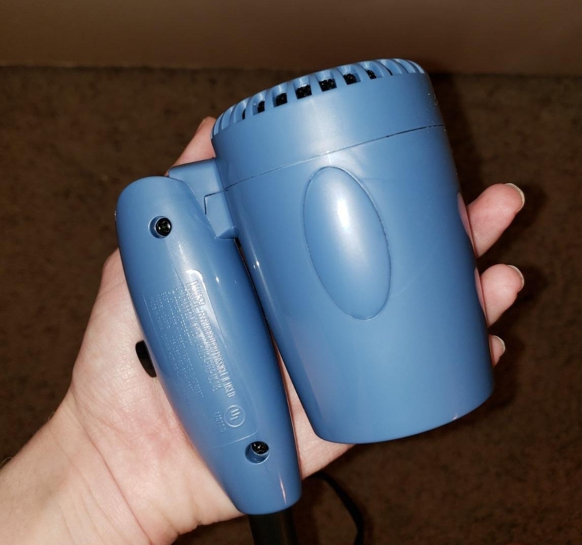 a reviewer holding the blue hair dryer folded in half in one hand