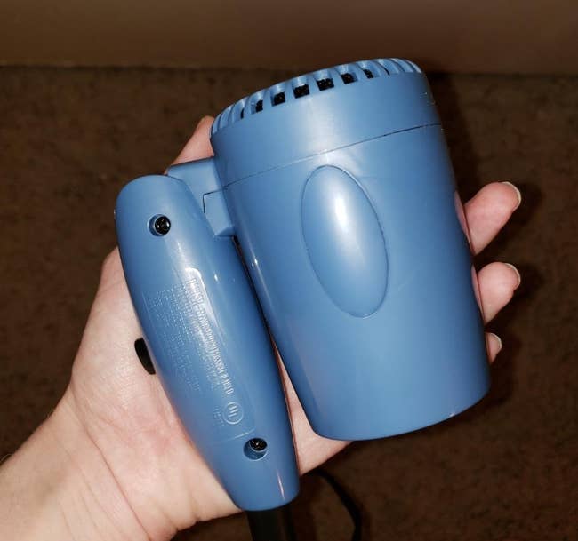 a reviewer holding the blue hair dryer folded in half in one hand