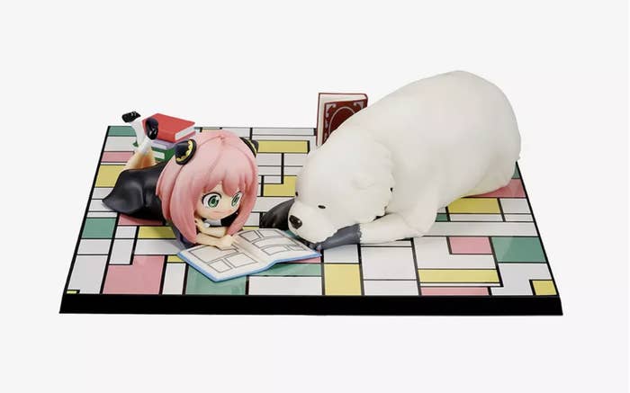Anime figure and bear-like plushie positioned on a checkered surface as if reading a book together.