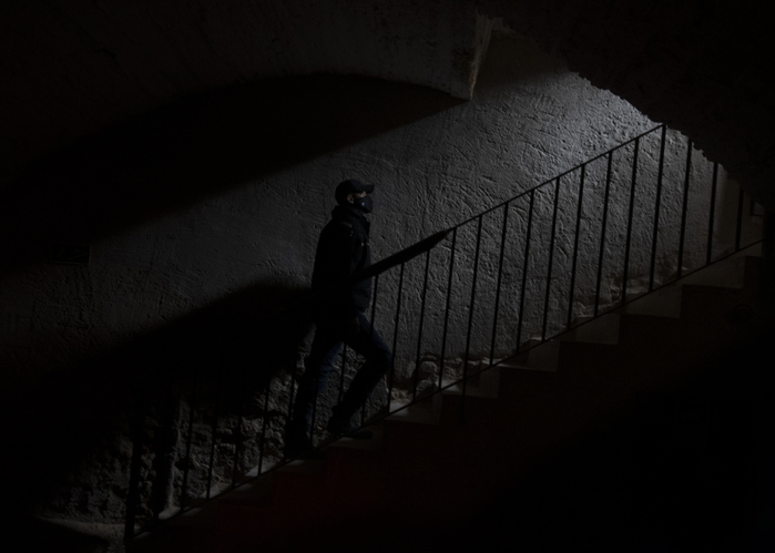 Person in silhouette ascending stairway with handrail, under an arch, in dim lighting