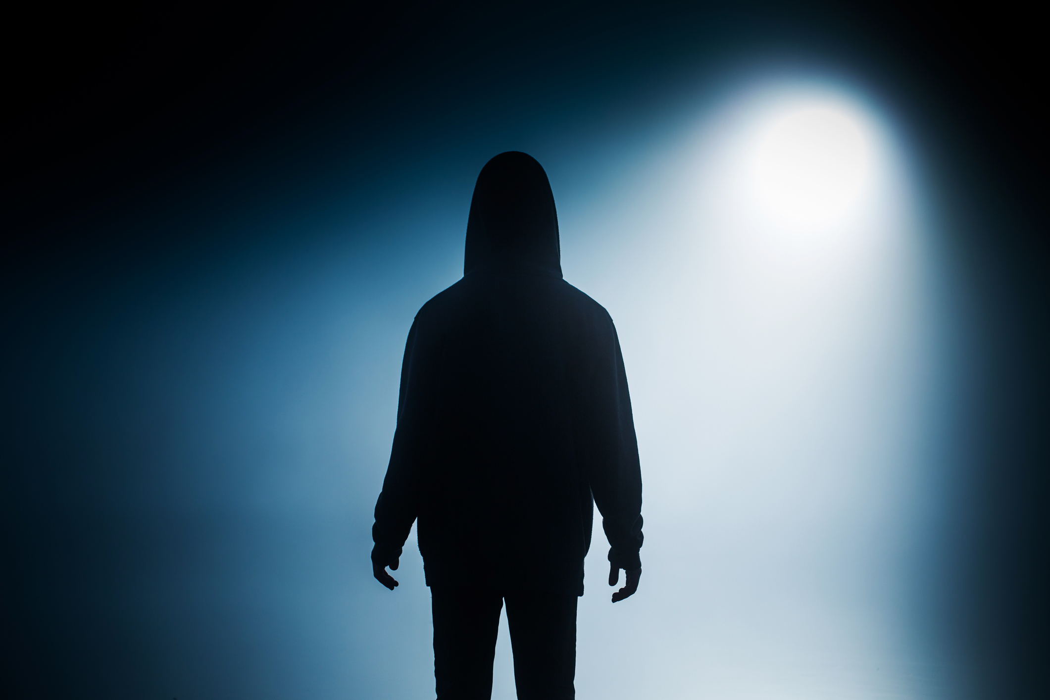Silhouetted figure standing against a bright light in a dark room, creating a mysterious atmosphere
