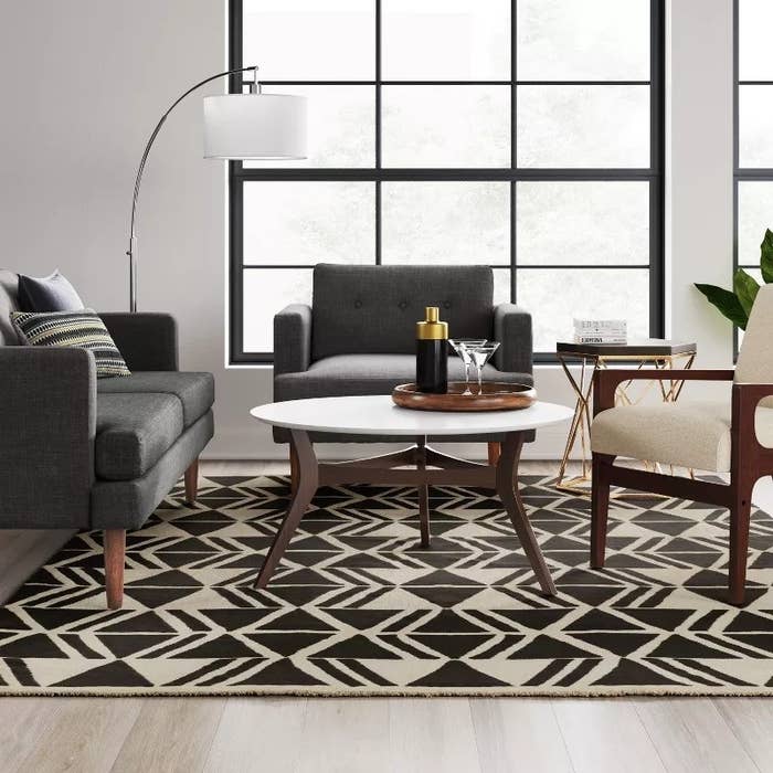 Modern living room with geometric rug, grey sofa, white coffee table, and gold accent decor