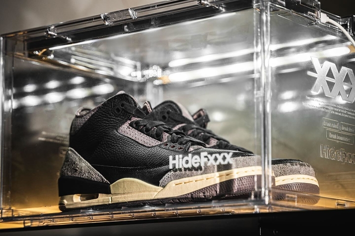 A pair of textured sneakers displayed in a clear acrylic case with branding on the front