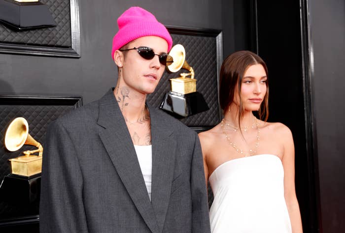 Justin Bieber in a pink beanie and suit with Hailey Bieber in a white off-shoulder gown at an event