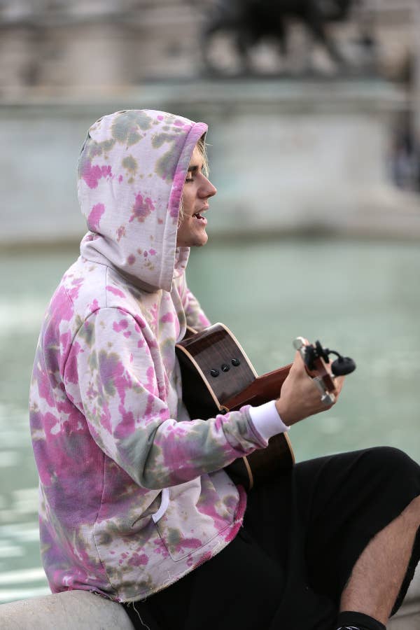 Person in a tie-dye hoodie playing the guitar outdoors