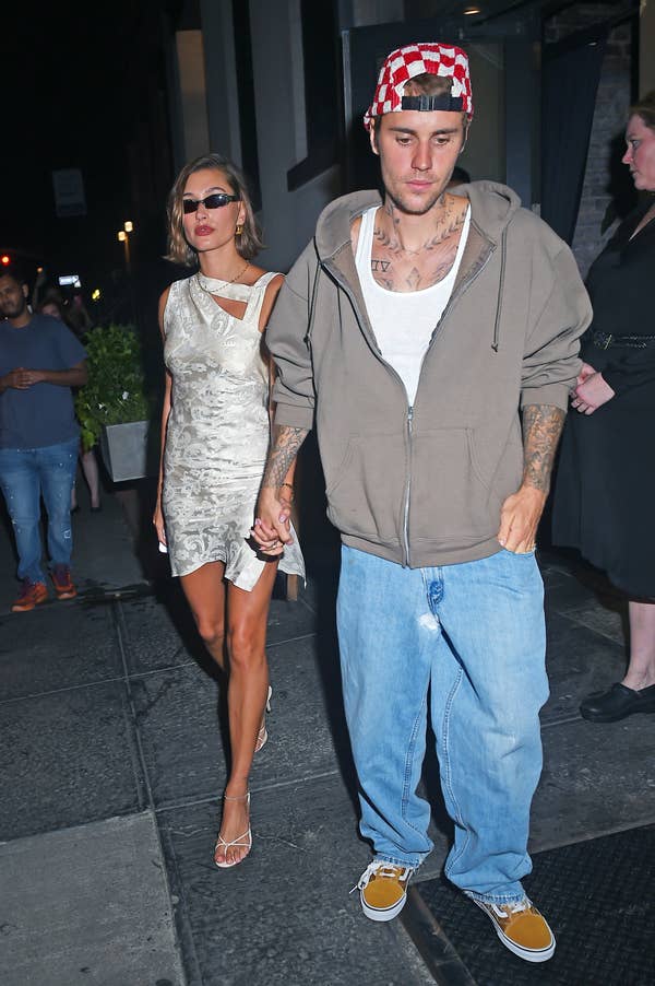 Woman in a metallic dress with a man in a hoodie and jeans, both holding hands on a city street at night