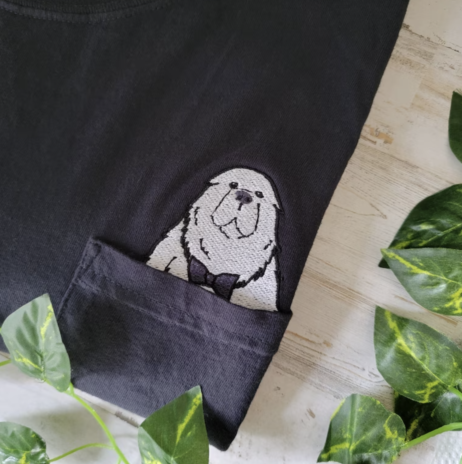 Black T-shirt with a graphic of a smiling dog, folded on a wooden surface with green leaves around