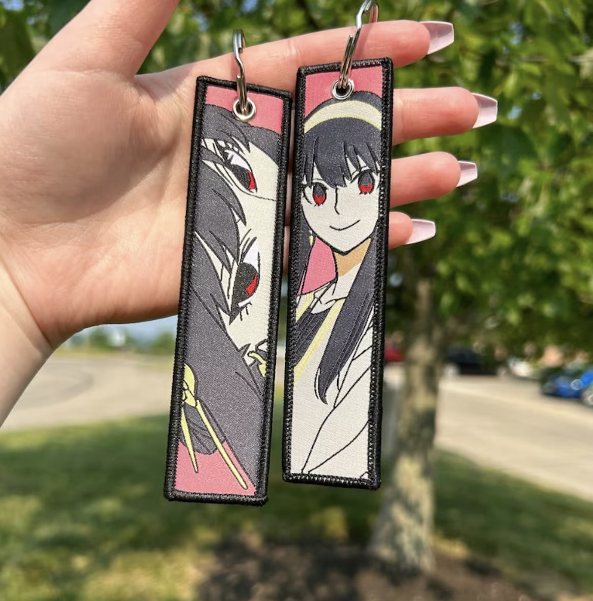 Person holding two anime character keychains outdoors