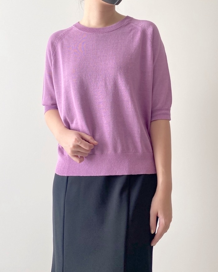Person in a purple sweater and black skirt, hand on hip, standing against a neutral background