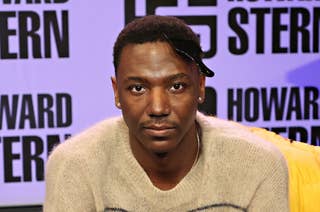 Jerrod Carmichael in a knit sweater with striped accents seated and looking at the camera