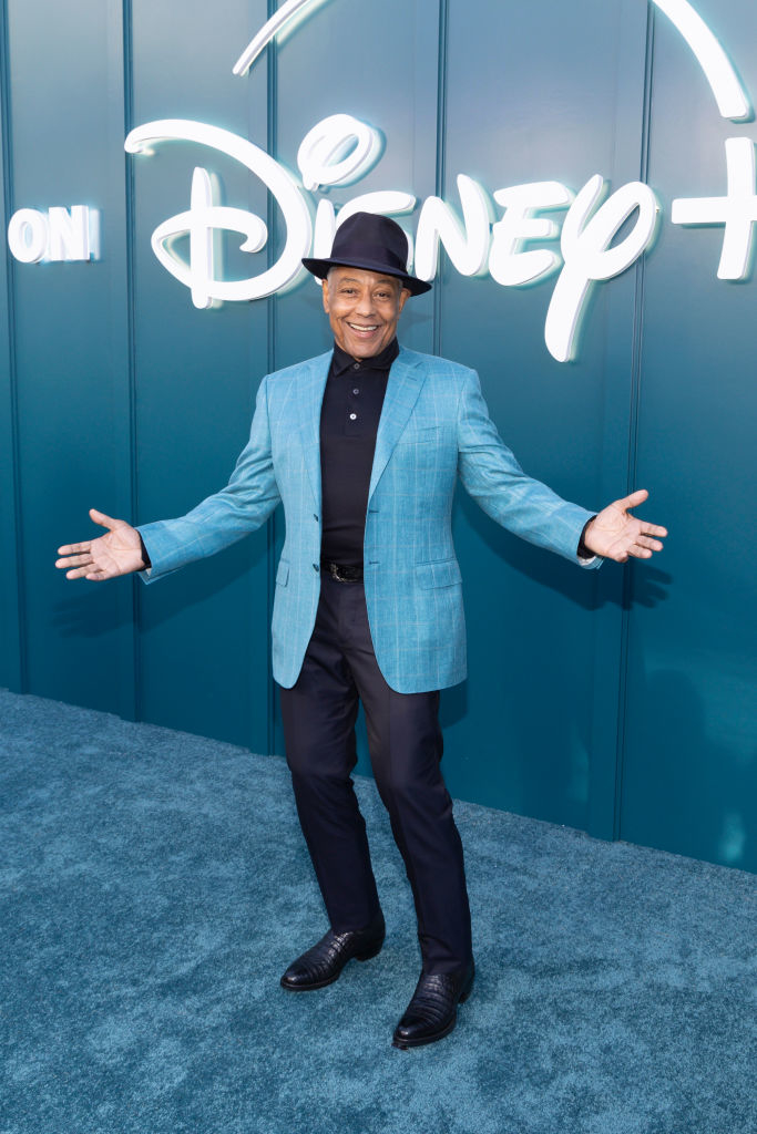 Giancarlo Esposito posing with arms outstretched wearing a light blazer and black pants at a Disney+ event