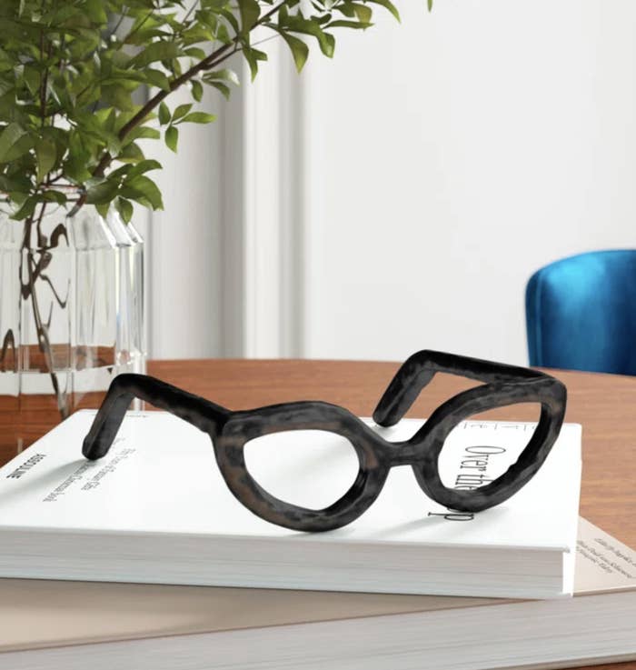 Oversized glasses sculpture on a book next to a plant on a desk