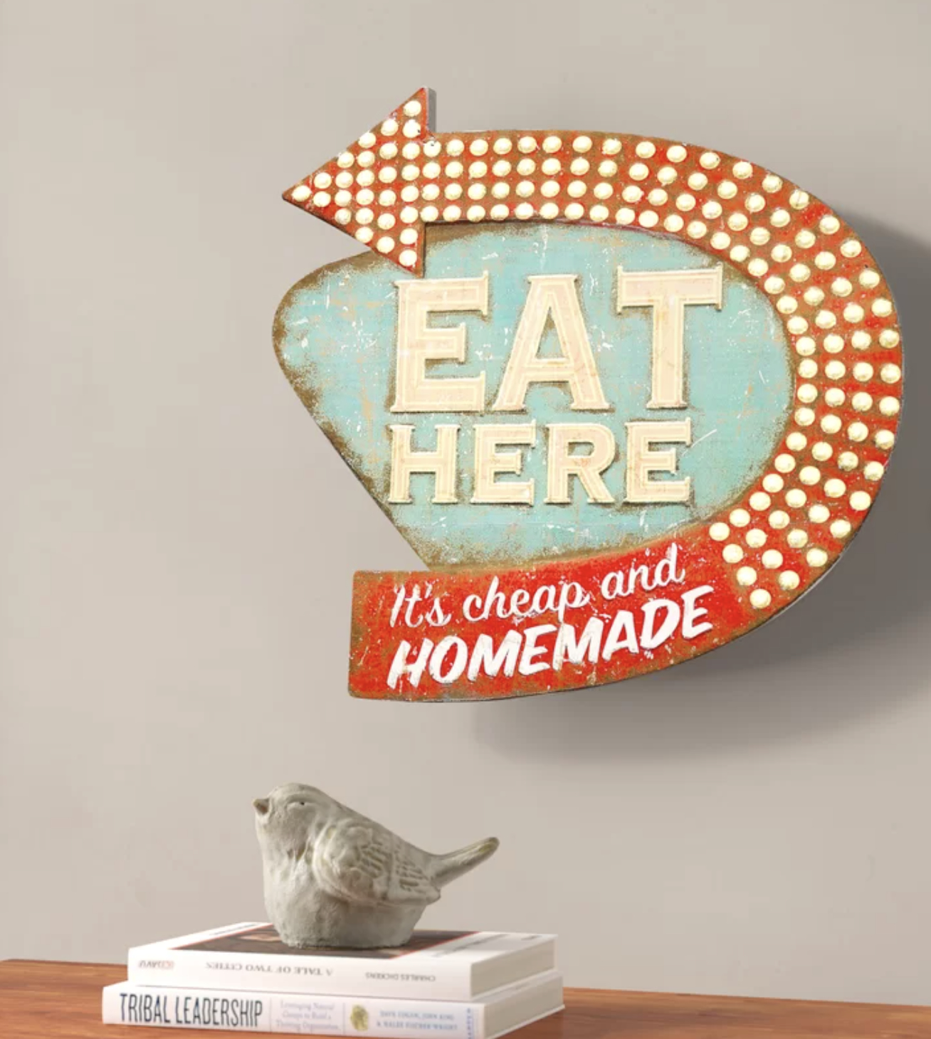 Vintage &quot;EAT HERE&quot; sign with arrow, perched atop books beside a bird figurine