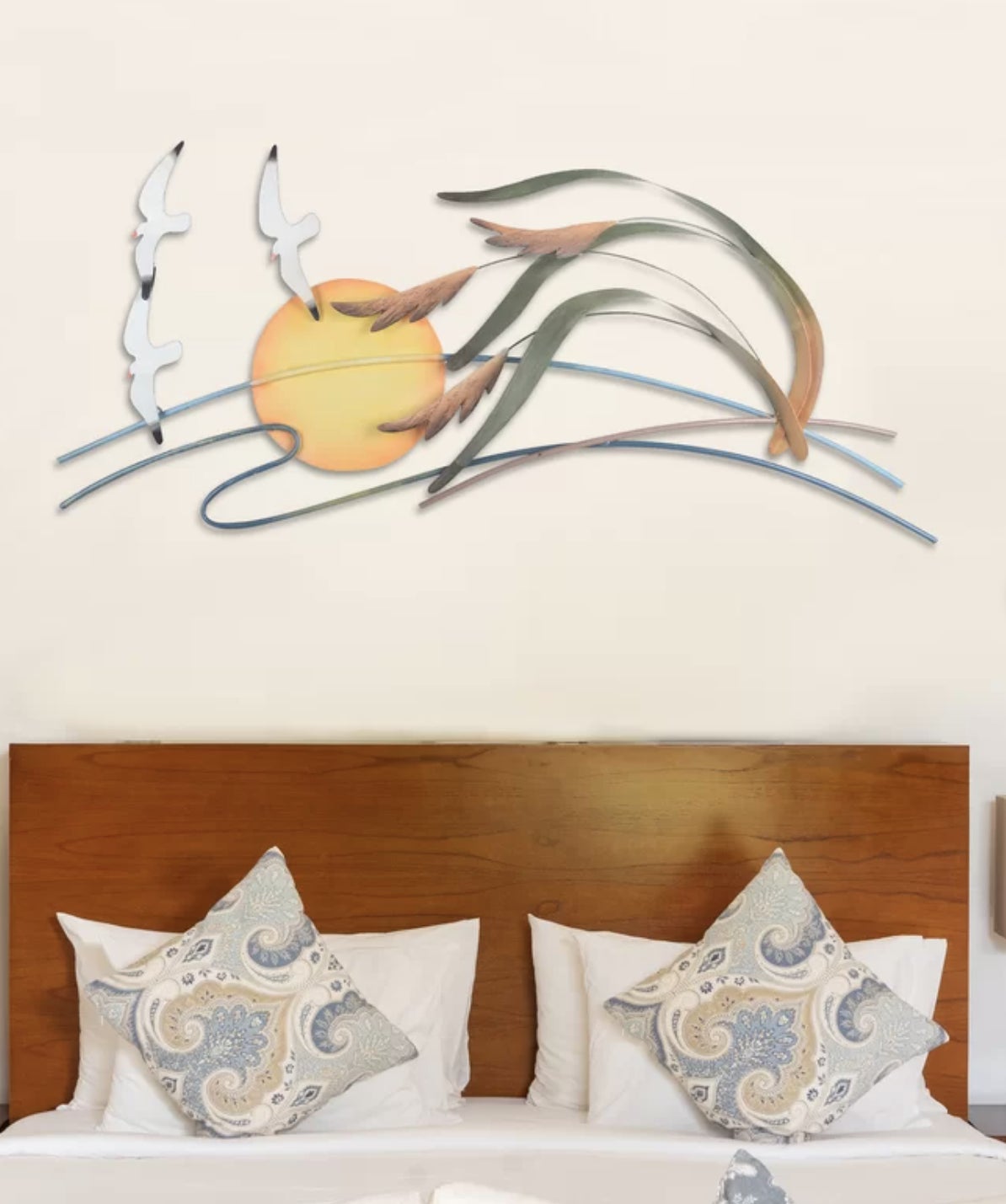 A decorative metal wall art piece featuring an abstract sun and waves design above a bed with two pillows