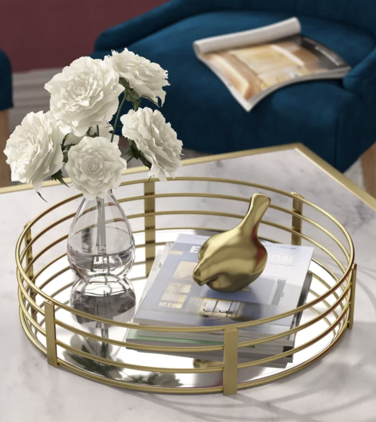 Decorative tray with a gold-tone figurine, white roses in a vase, and magazines on a table