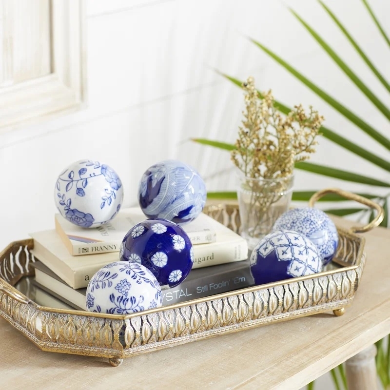 A decorative tray with blue and white ornamental spheres on stacked books, next to a vase with dried flowers