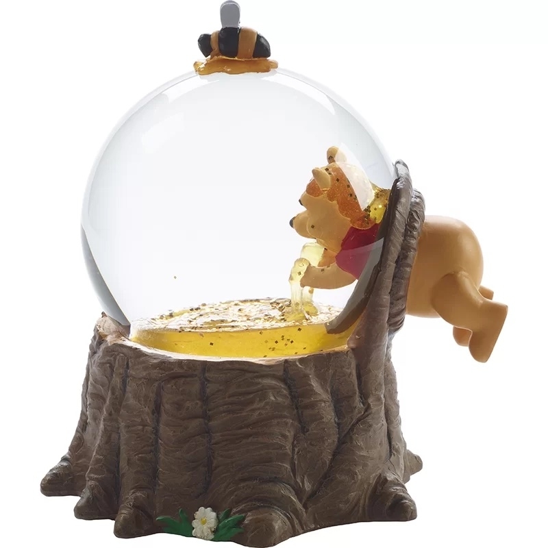 Winnie the Pooh figurine reaching into a honey pot snow globe on a tree stump base