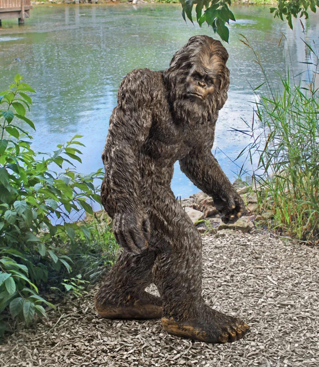 Figure of Bigfoot by a pond with greenery in the background