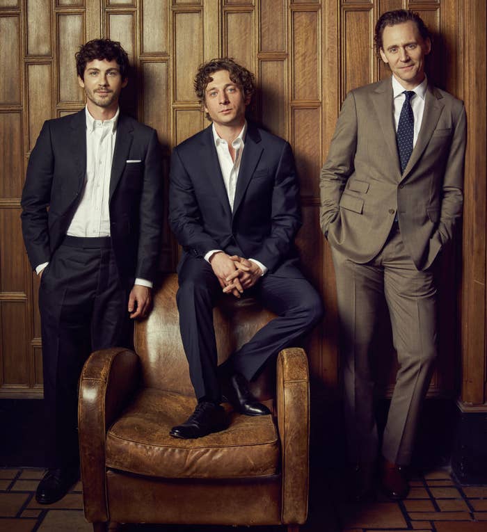 Logan Lerman, Jeremy Allen White, and Tom Hiddleston in suits, posing with one seated and two standing, all looking at the camera
