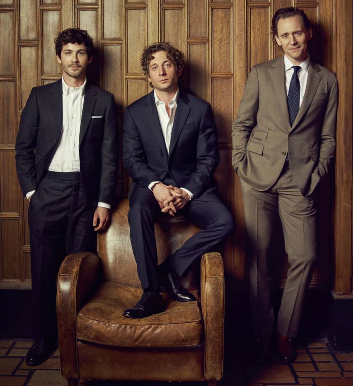 Logan Lerman, Jeremy Allen White, and Tom Hiddleston in suits, posing with one seated and two standing, all looking at the camera