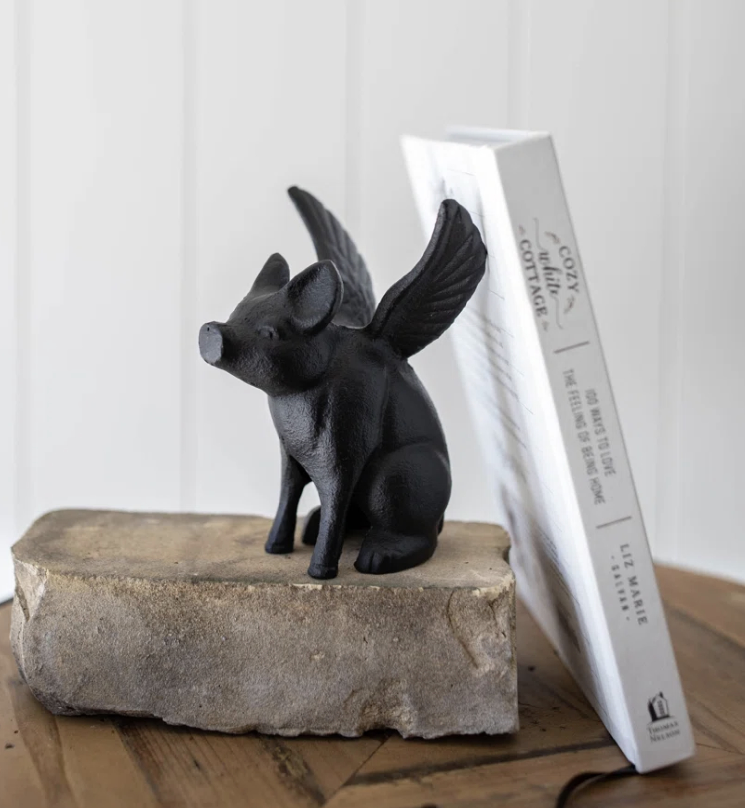 A winged pig figurine sits on a stone beside a propped book