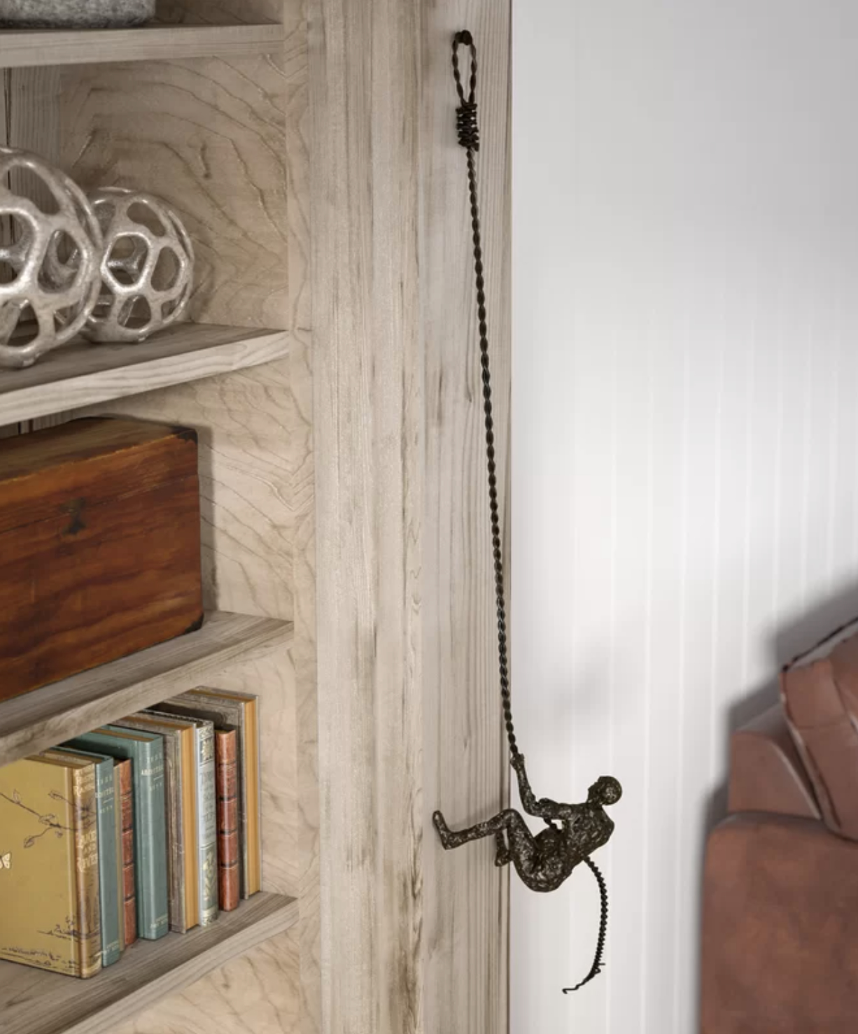 Decorative wall-mounted metal figure of a climber ascending, next to a bookshelf and sofa