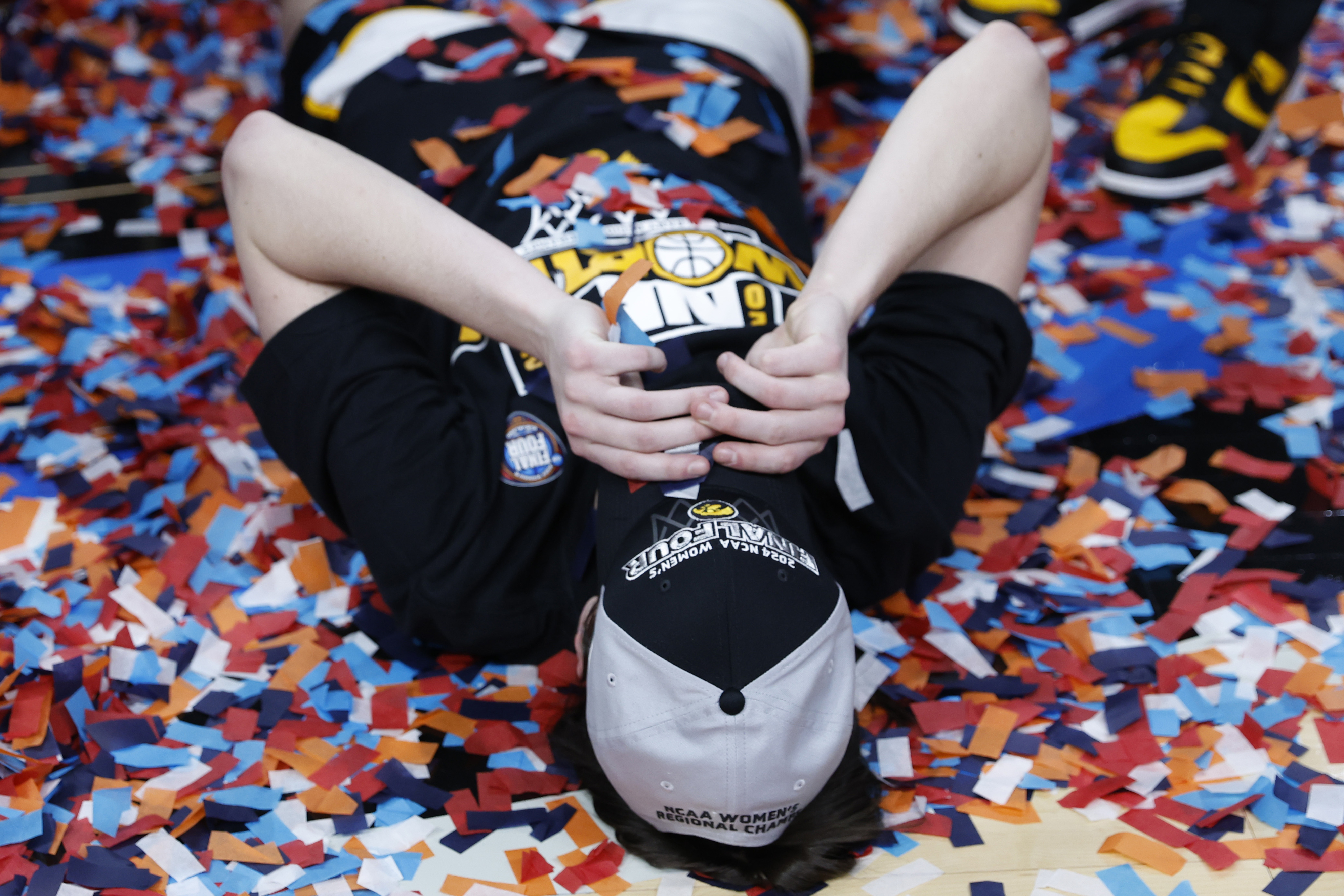 Person lying on the floor with confetti, hands behind head, celebrating a basketball victory